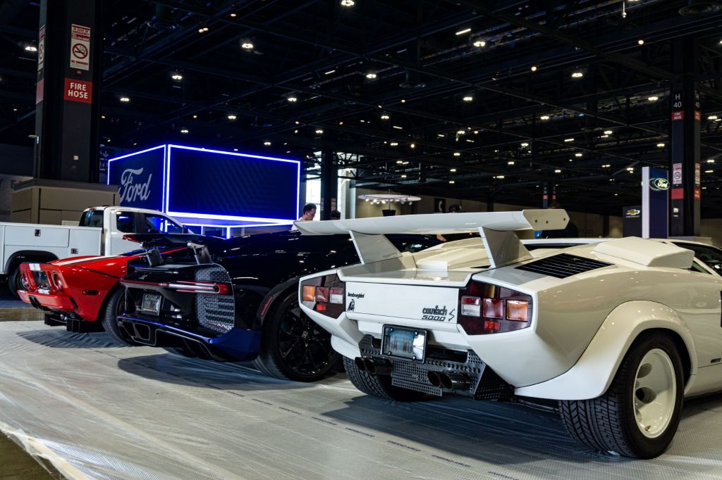 The rear 3/4 view of a white Lamborghini Countach 5000 S, black-and-blue Bugatti Chiron, and red-and-white Ford GT at the 2021 Chicago Auto Show