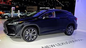 A dark blue Lexus RX sitting in a showroom with other cars behind it on a white floor with black lettering stating "New Lexus RX 450h" on the floor.