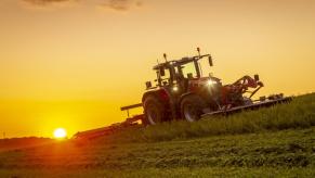 A Massey Ferguson 8S tractor working a hay field at sunrise