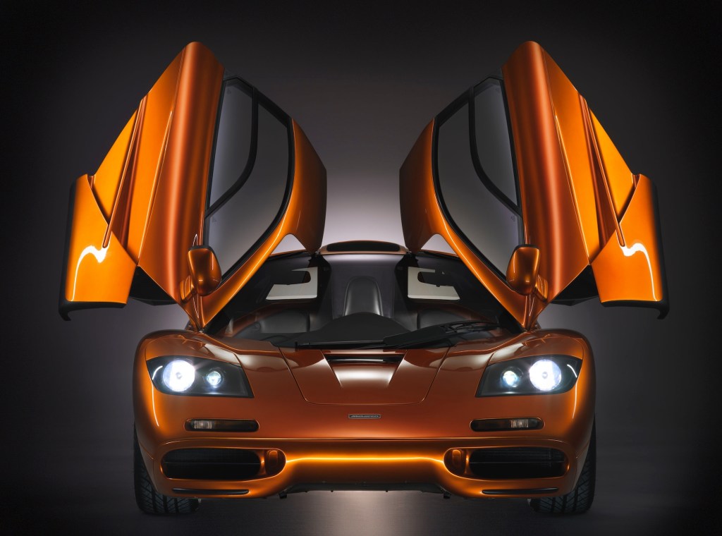 A head-on view of an orange metallic McLaren F1 supercar with its gull-wing doors open