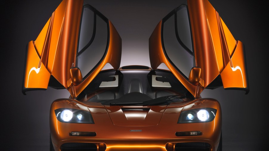 A head-on view of an orange metallic McLaren F1 supercar with its gull-wing doors open