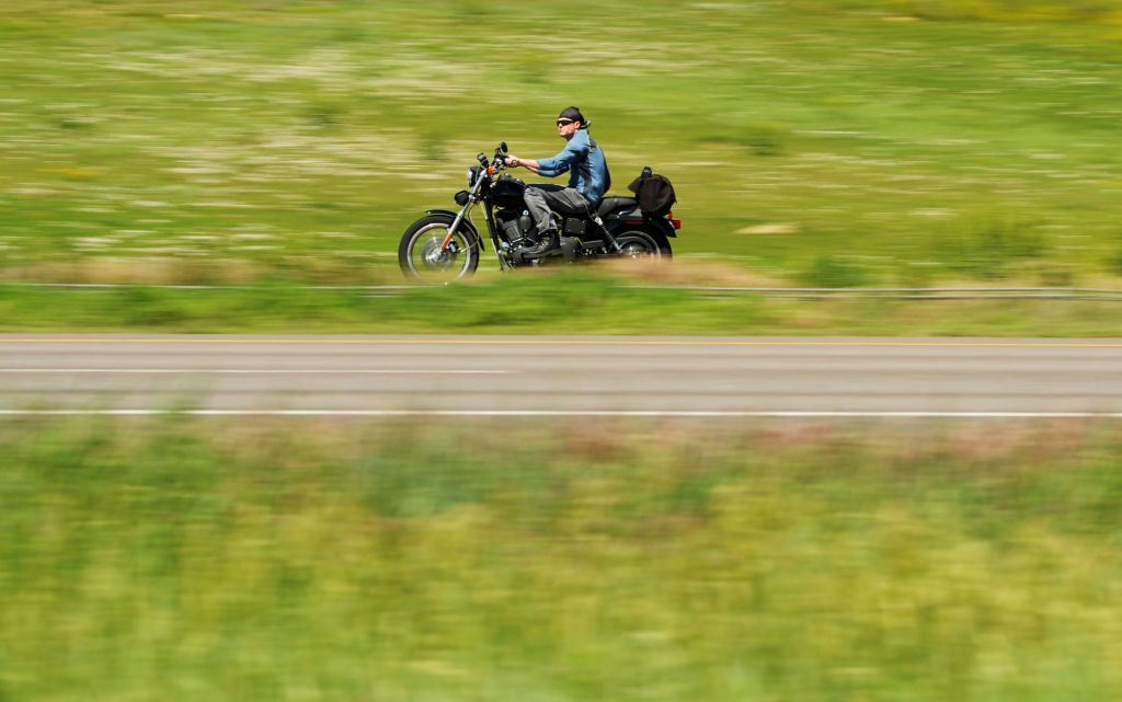 A man driving a motorcycle on the highway near grass fields and hills