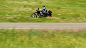A man driving a motorcycle on the highway near grass fields and hills