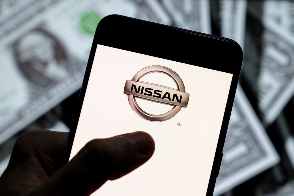 Photo illustration of the Nissan logo displayed on a smartphone screen with U.S. dollar bills in the background