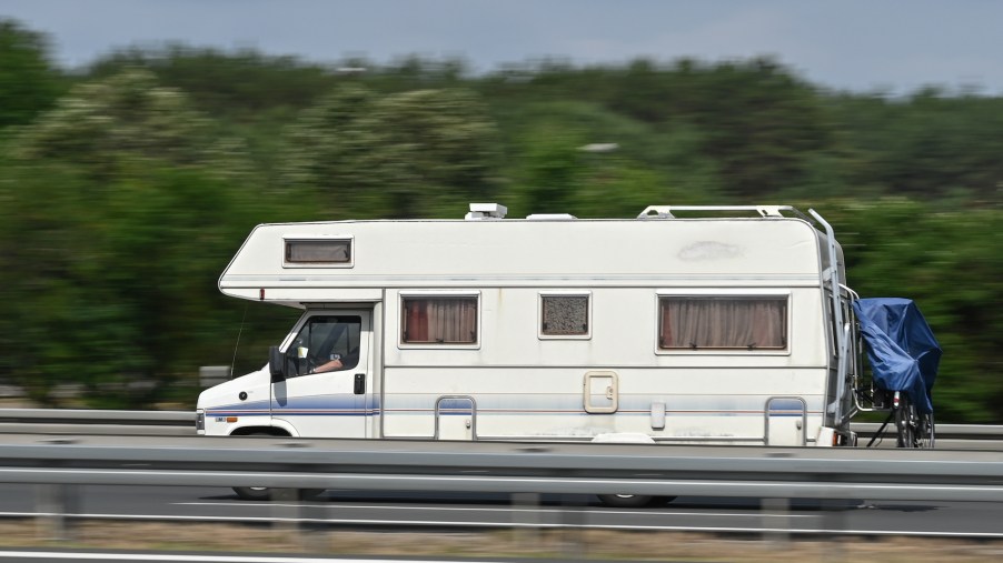 An RV travels on a road along a guardrail and trees