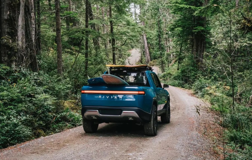 Rivian R1T driving through the woods with surfboards in the back