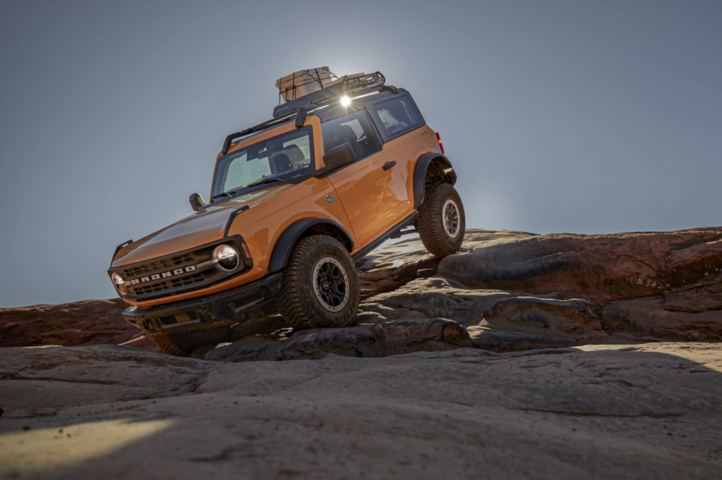 A yellow 2021 Ford Bronco off-roading over rocks serves as a reminder that this is the coolest car you can buy right now with one bitcoin