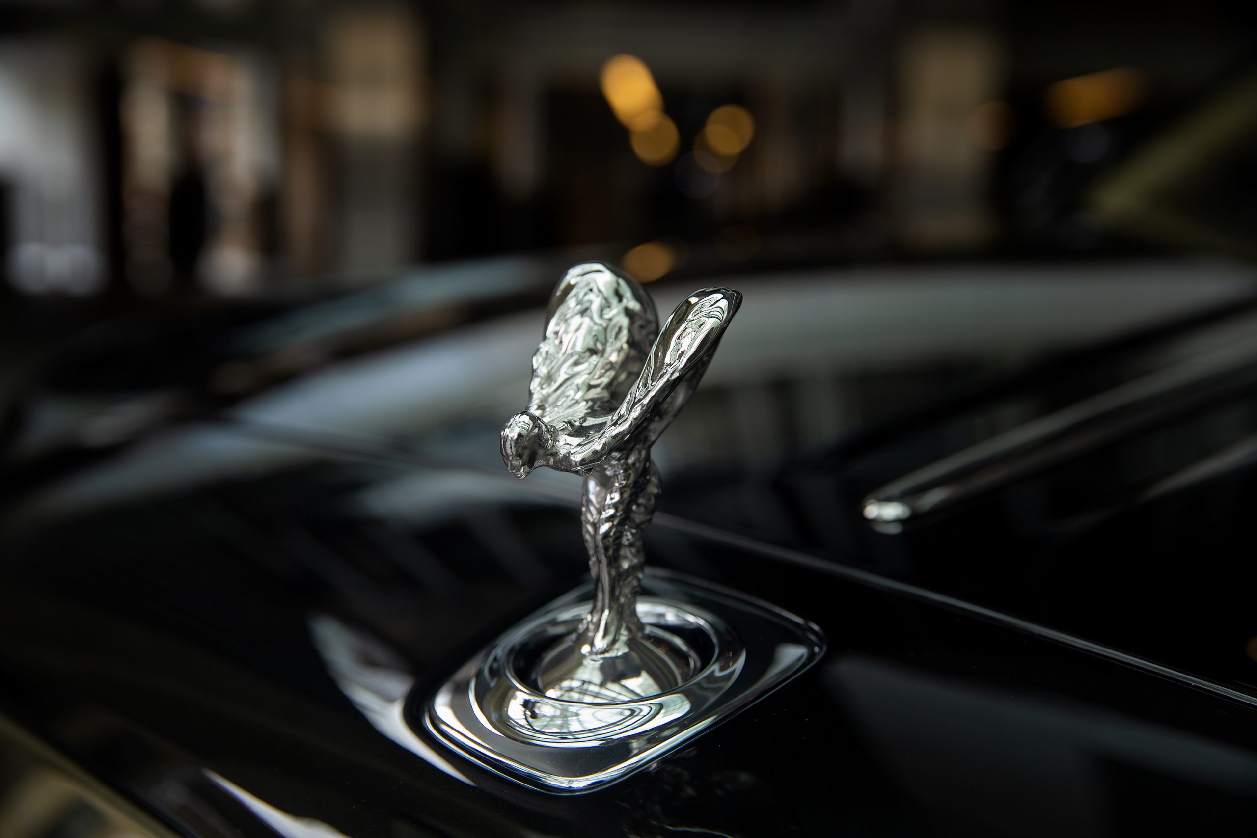 A silver Spirit of Ecstasy hood ornament on a black Rolls-Royce