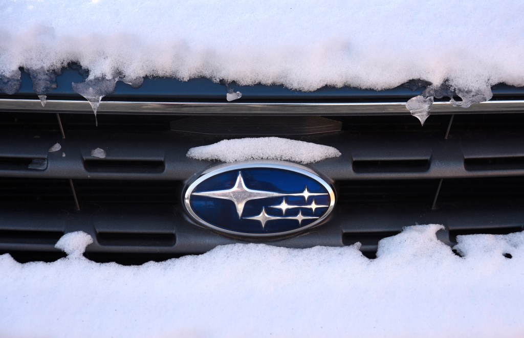 A snow-covered Subaru logo badge on the front grille of a car