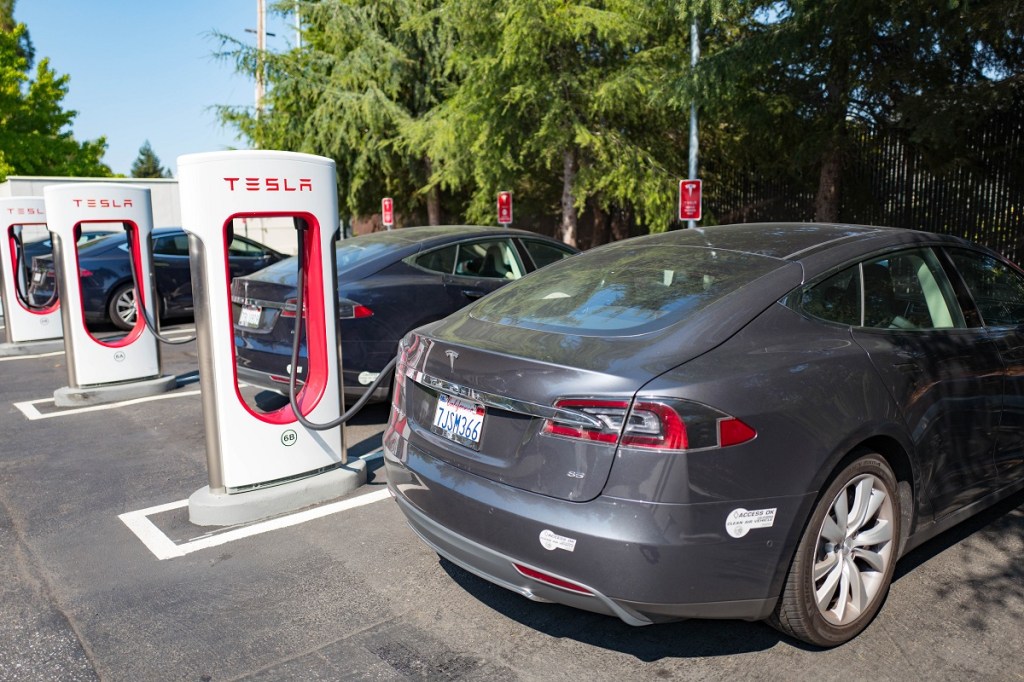 Tesla vehicles are plugged in and charging at a Supercharger rapid battery charging station