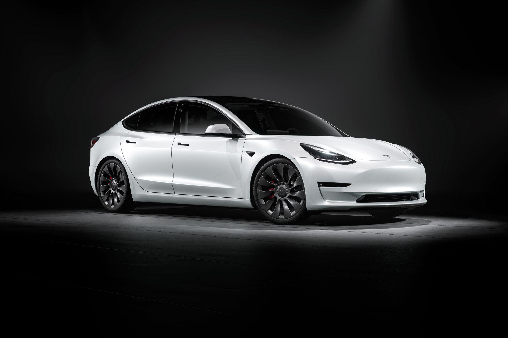 A white Tesla highlighted with a spotlight with black floors and walls.