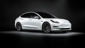 A white Tesla highlighted with a spotlight with black floors and walls.