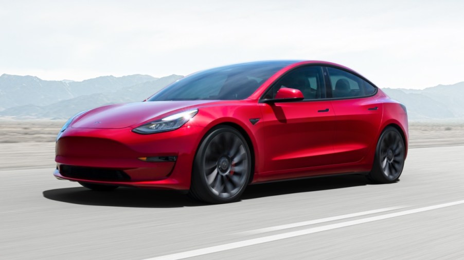A red 2021 Tesla Model 3 driving down a highway.