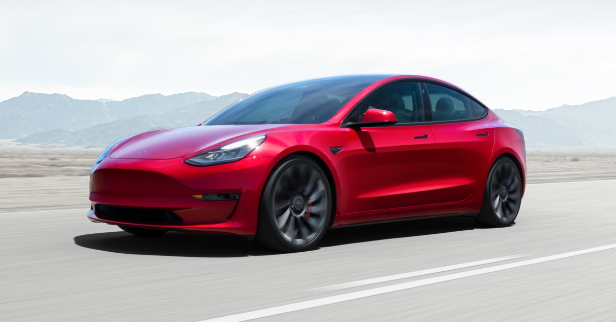 A red 2021 Tesla Model 3 speeds down the highway.