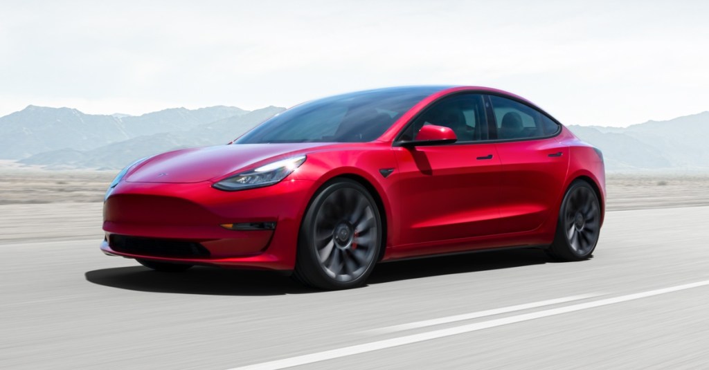 A red 2021 Tesla Model 3 speeds down a highway.
