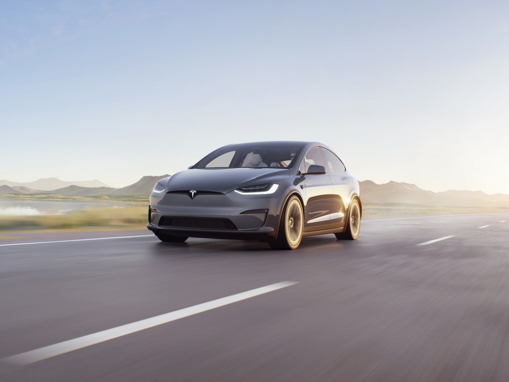 A dark Tesla Model X driving down an empty road with the sun shining behind it, the Tesla Model X is a Tesla SUV and is the first Tesla car 'Ted Lasso' star Jason Sudeikis has ever owned