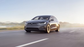 A dark Tesla Model X driving down an empty road with the sun shining behind it, the Tesla Model X is a Tesla SUV and is the first Tesla car 'Ted Lasso' star Jason Sudeikis has ever owned