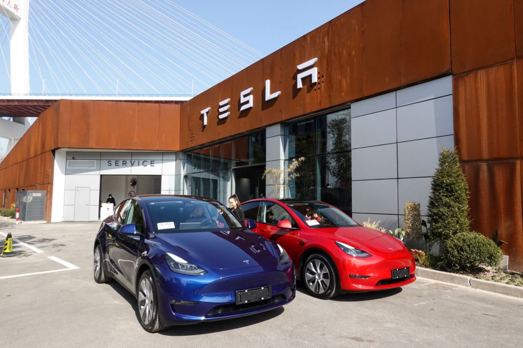 A pair of blue and red Tesla models parked outside of a Tesla showroom building