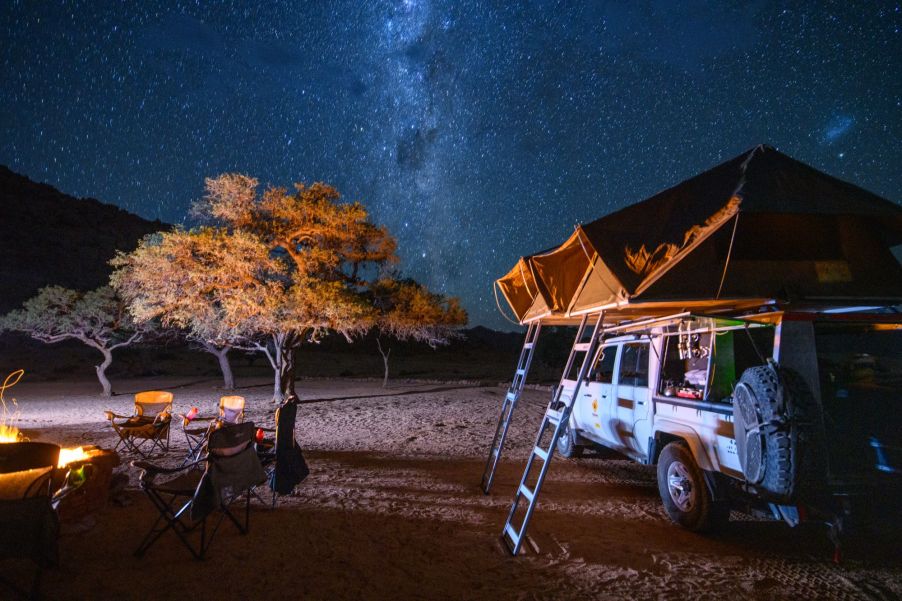 A truck bed tent set up near a campsite with a fire and a starry night sky