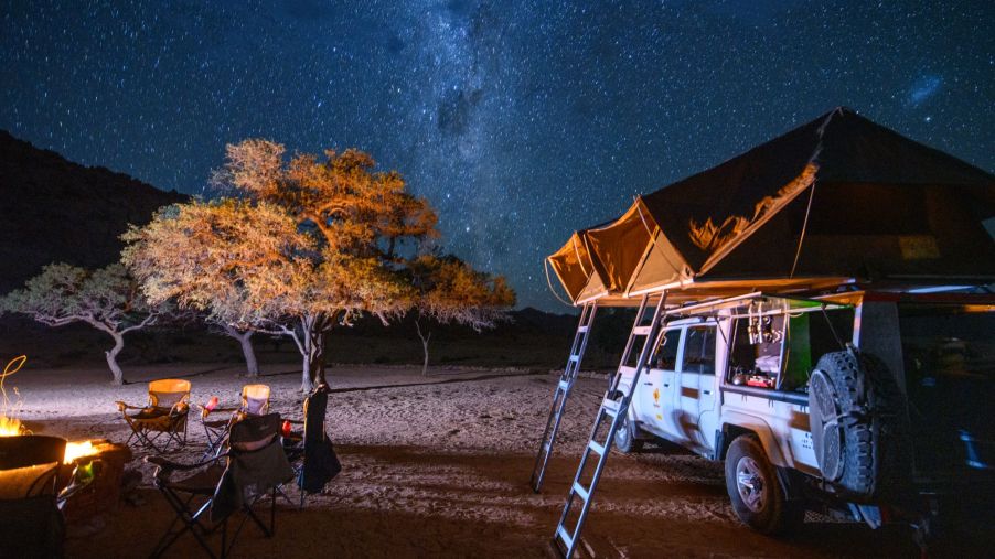 A truck bed tent set up near a campsite with a fire and a starry night sky