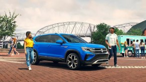 A bright blue 2022 Volkswagen Taos parked in front of a bridge.