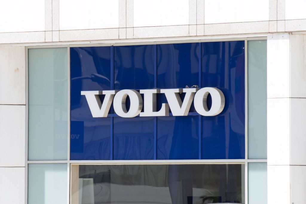 A large blue sign with 'Volvo' printed framed by a white section of what looks like a building with a glass window underneath the sign.