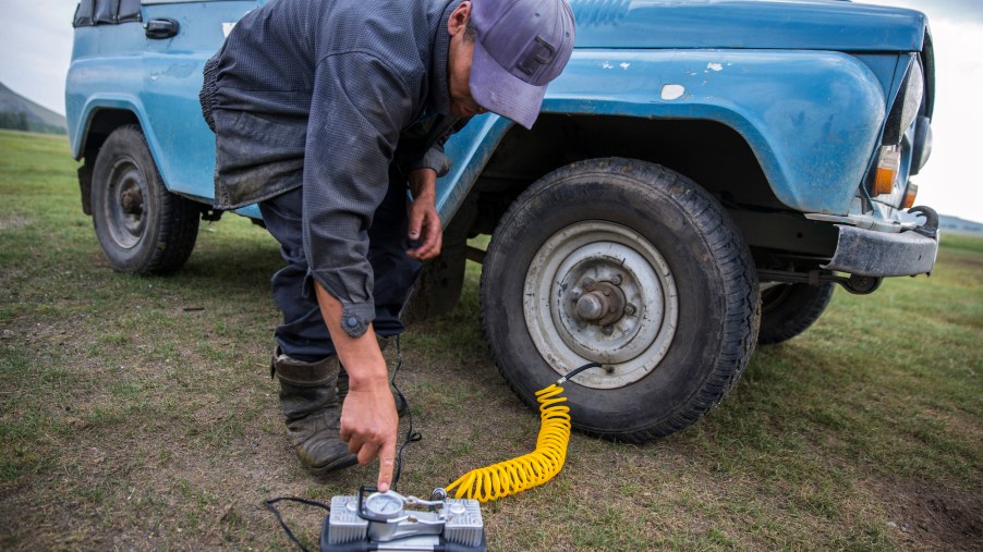 A man turns on a battery-powered air compressor whose hose is attached to his SUV's right front tire