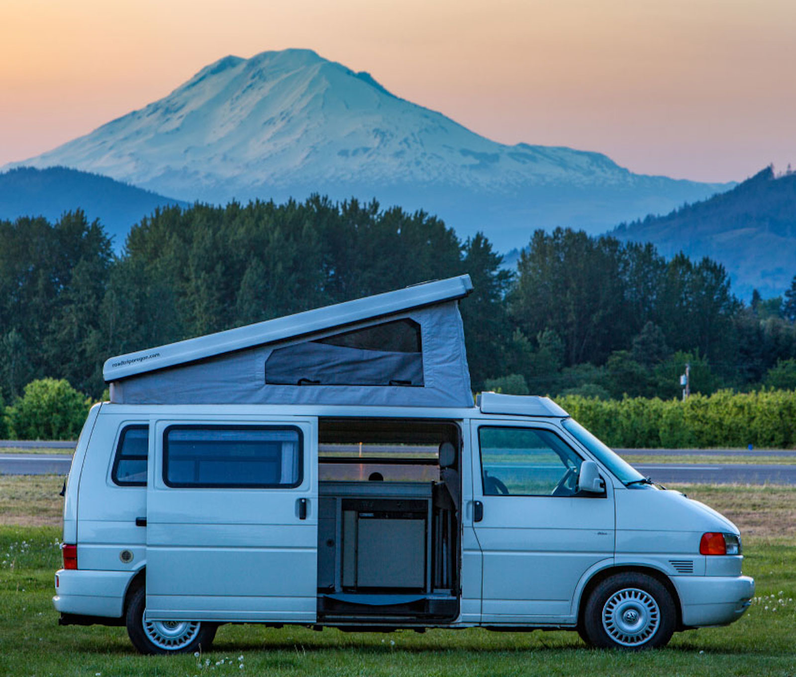 A Volkswagen European parked in a field at dusk with a mountainous backdrop and the pop top open