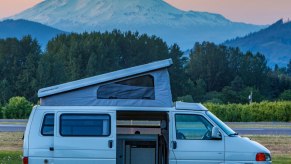 A Volkswagen European parked in a field at dusk with a mountainous backdrop and the pop top open