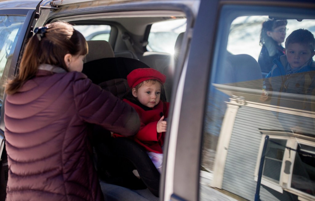 Hannah DeWick, 15, straps her newly adopted sister, Paisley, 2, into her car seat in a minivan in Rockport, Maine
