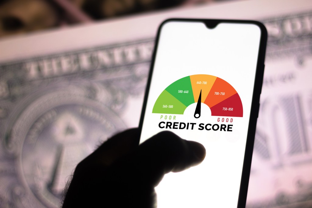 A photo illustration of a hand holding a smartphone showing a graph with the credit score