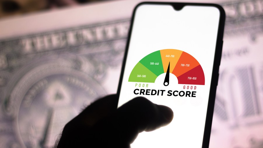 A photo illustration of a hand holding a smartphone showing a graph with the credit score