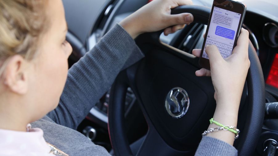 A young woman texts on her phone while driving, the biggest driving distraction
