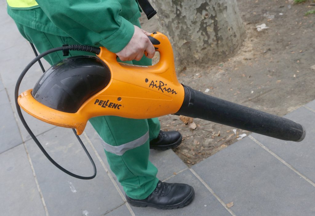 A maintenance employee uses an electric handheld leaf blower