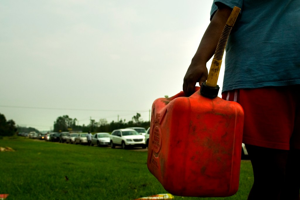 A person carrying a red plastic gas can on the side of the road