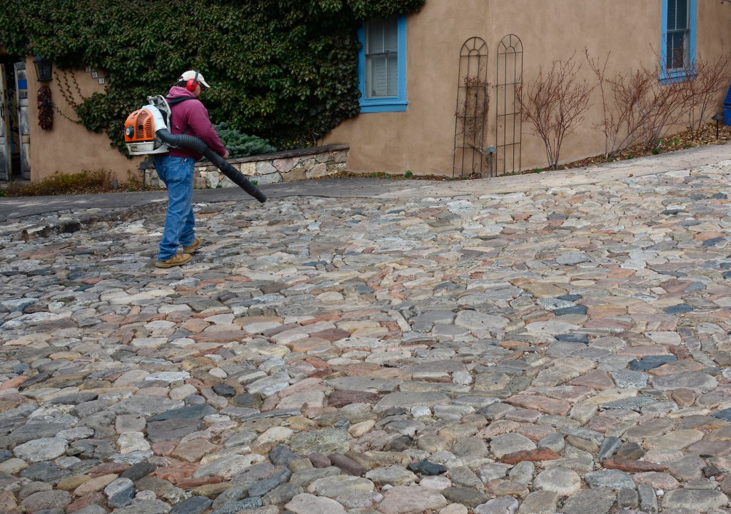 A man uses a gas-powered backpack leaf blower to clean up a yard in Santa Fe, New Mexico