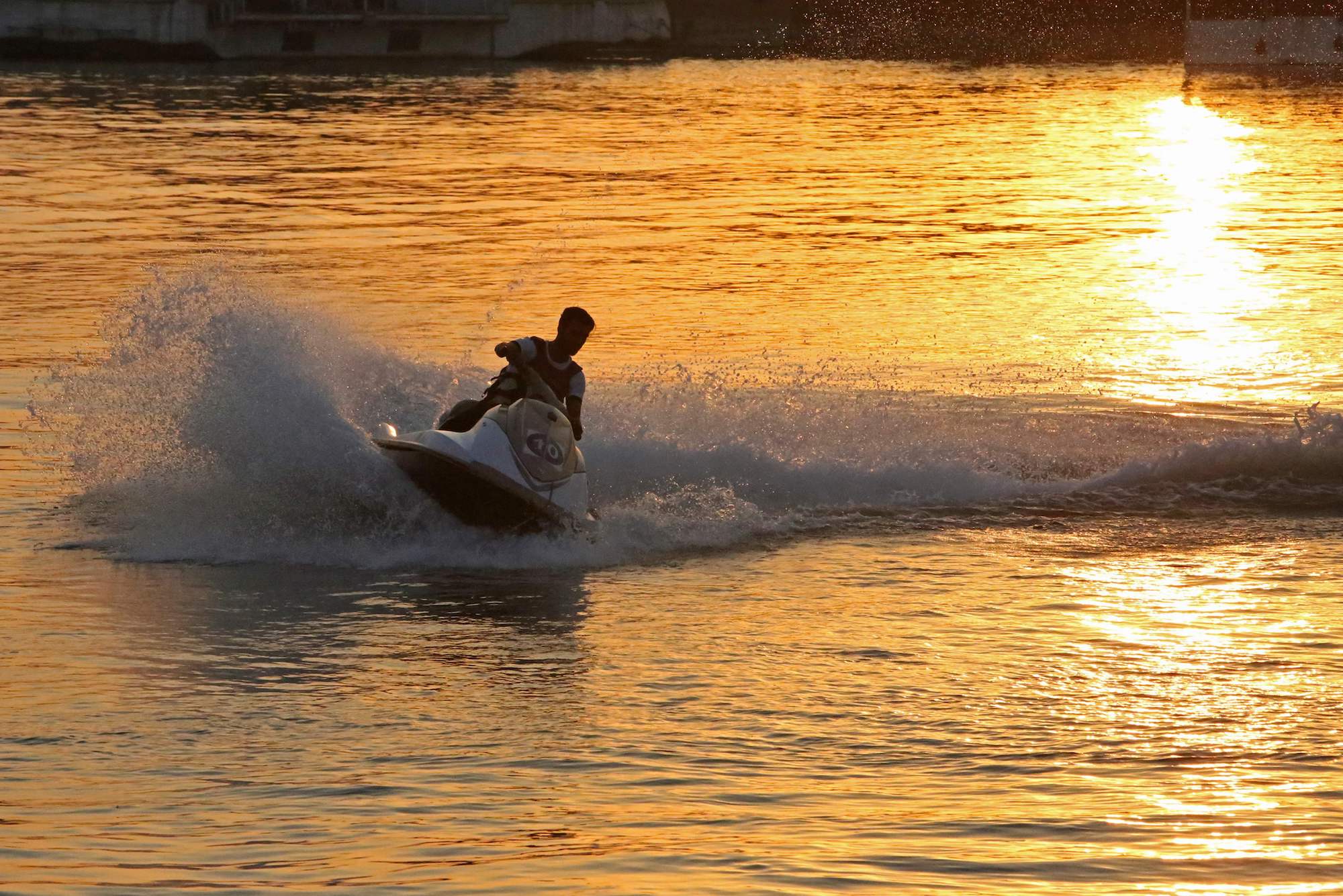 A person rides a jet ski on a river at sunset