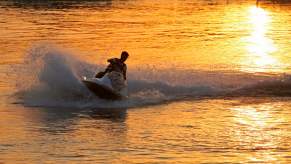 A person rides a jet ski on a river at sunset