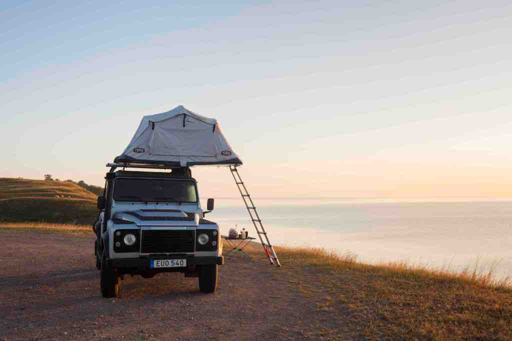 Off-road four-wheel-drive vehicle with rooftop tent camping along the Baltic Sea. 