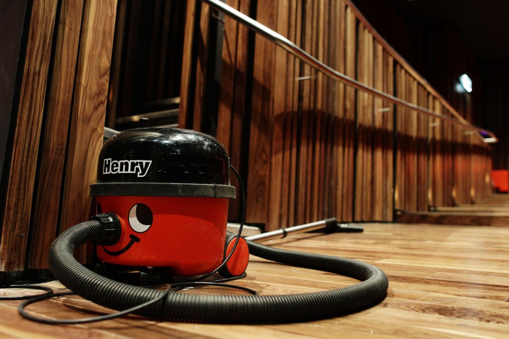 A shop vac sits on a wood floor in a wood-paneled auditorium