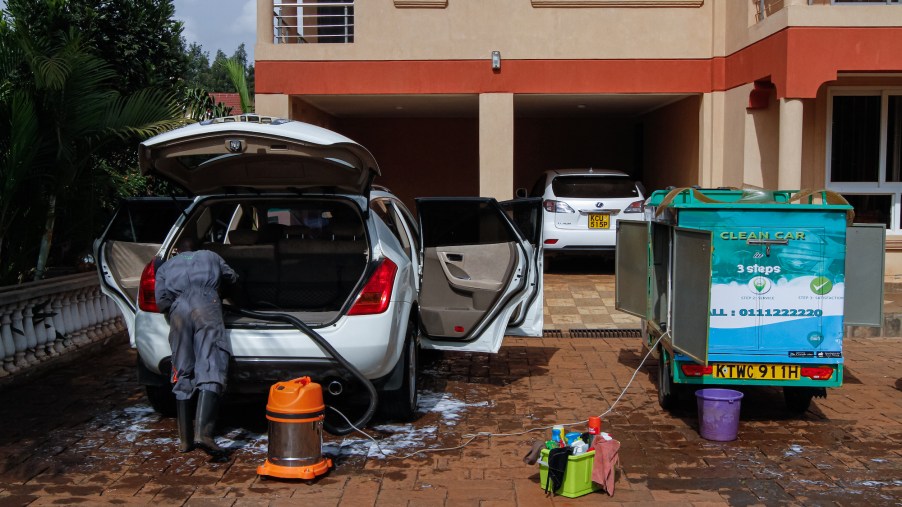 A mobile car wash worker uses a shop vac to vacuum the back of an SUV in a customer's front yard