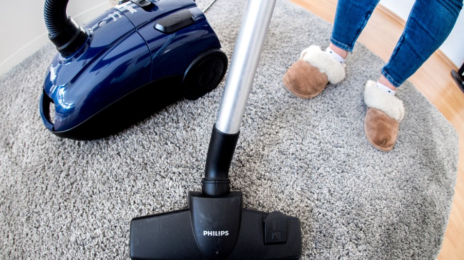 A woman in an apartment uses a vacuum cleaner on carpeting