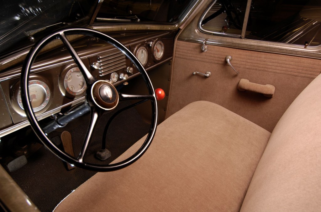 The interior of a 1937 Oldsmobile featuring its steering wheel, transmission, dashboard, and upholstery