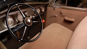 The interior of a 1937 Oldsmobile featuring its steering wheel, transmission, dashboard, and upholstery