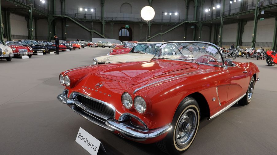A red 1962 Chevrolet Corvette sitting in a large building with high ceilings with other classic cars.