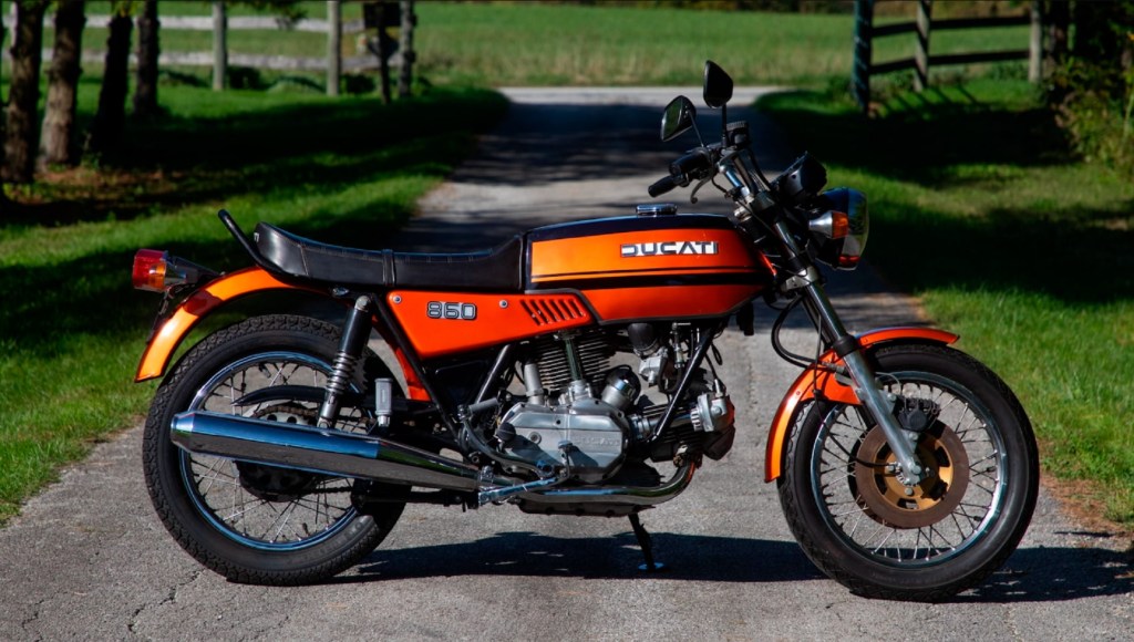 The side view of an orange 1975 Ducati 860 GT on a grassy dirt road