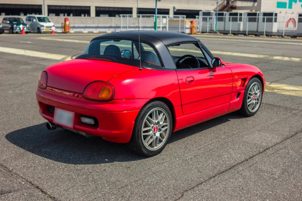 The rear 3/4 view of a red 1993 Suzuki Cappuccino with a black roof in a parking lot