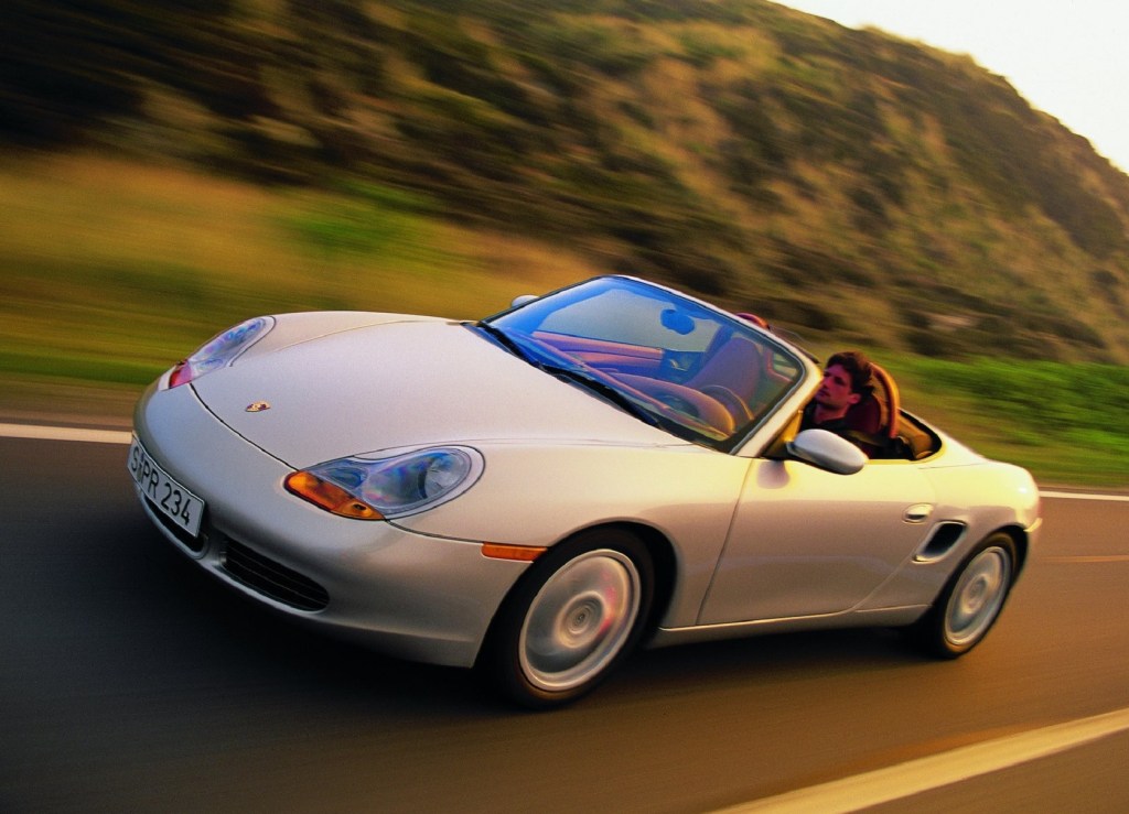 A silver 2001 Porsche Boxster S driving down a road ringed by hills