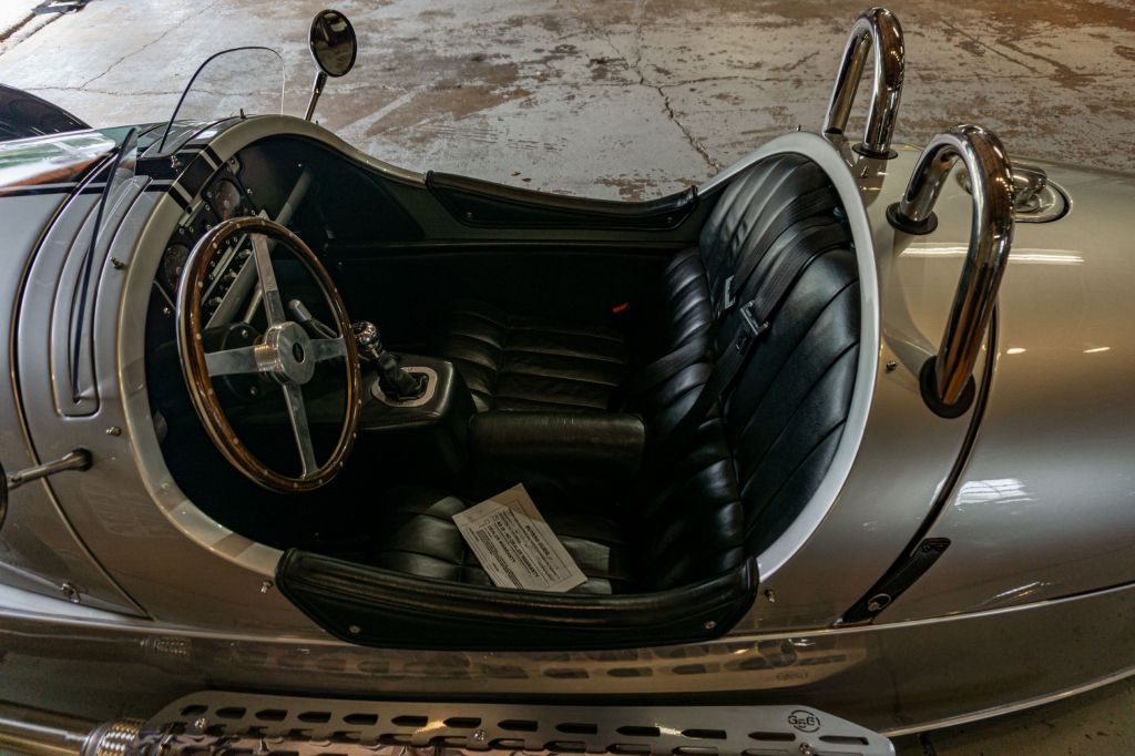 The black-leather-upholstered cockpit of a silver 2012 Morgan 3-Wheeler in a garage