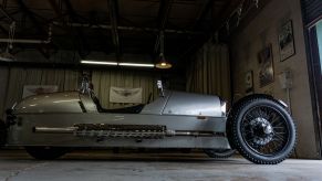 A low-angle side view of a silver 2012 Morgan 3-Wheeler in a garage